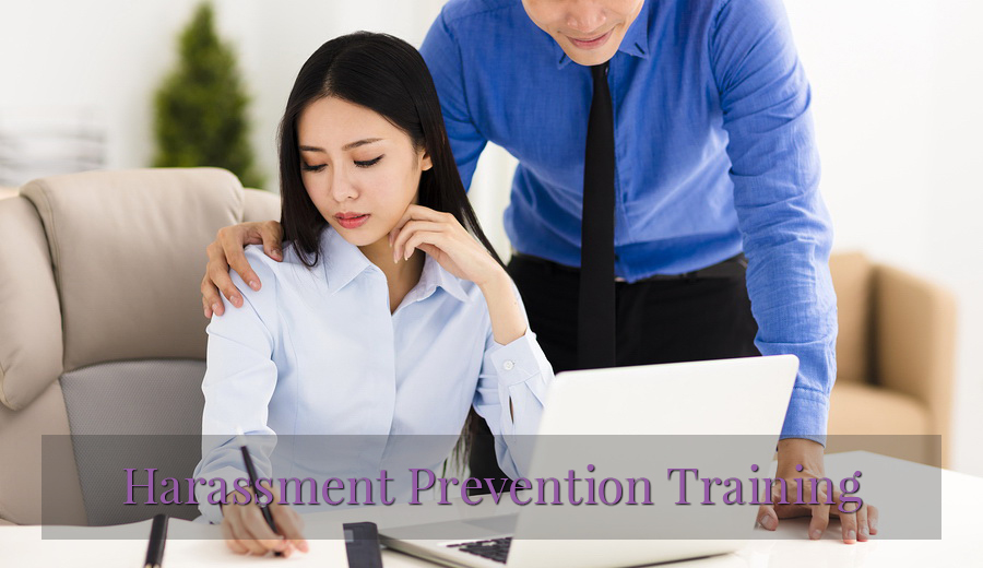 A young businessman in a blue shirt stands behind a woman in a white shirt writing on a notepad, addressing sexual harassment prevention training in the workplace.