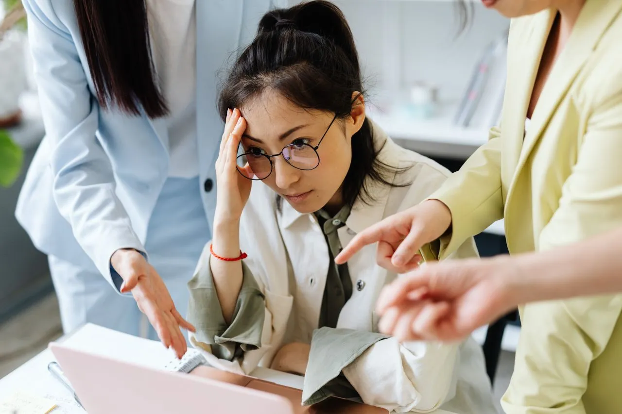 A stressed woman and coworkers in a tense office meeting for Toxic Workplace Training.